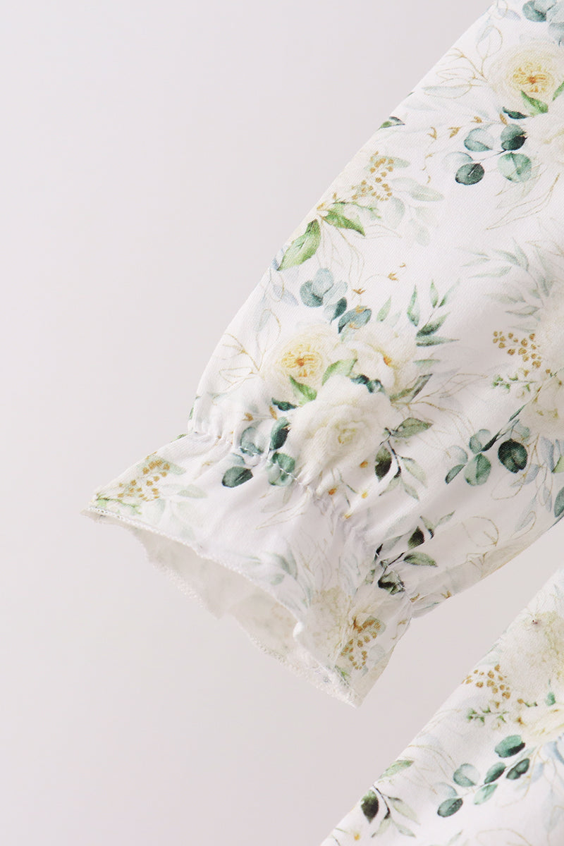 A close-up of a white fabric sleeve or garment section with a delicate floral print in soft green, cream, and muted yellow, featuring ruffled trim along one edge.