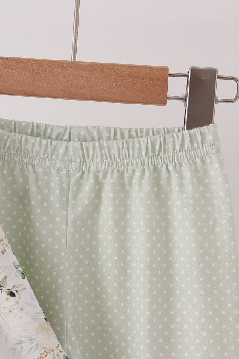Sage green polka dot pants with smocked elastic waistband hanging on wooden hanger, featuring floral print detail.