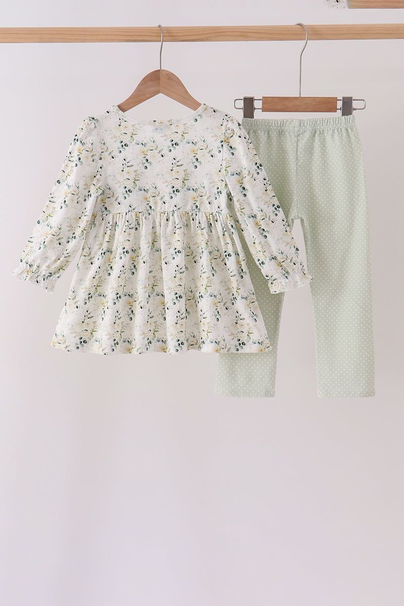 White floral printed tunic with ruffled sleeves hangs beside sage green polka dot pants, a charming two-piece kids set.