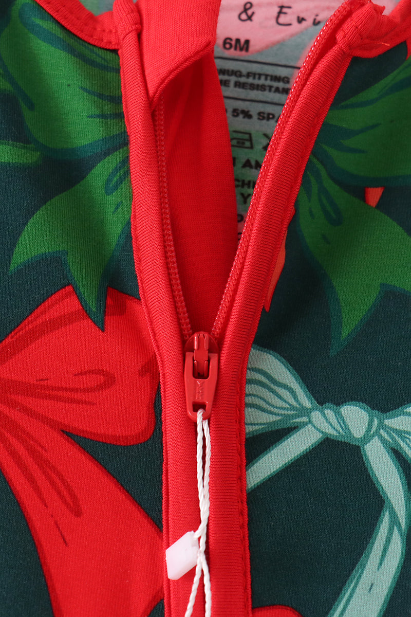 Close-up of a children's zip-up garment with a red zipper and trim, featuring a festive holiday print with red bows and green leaves on a dark background.