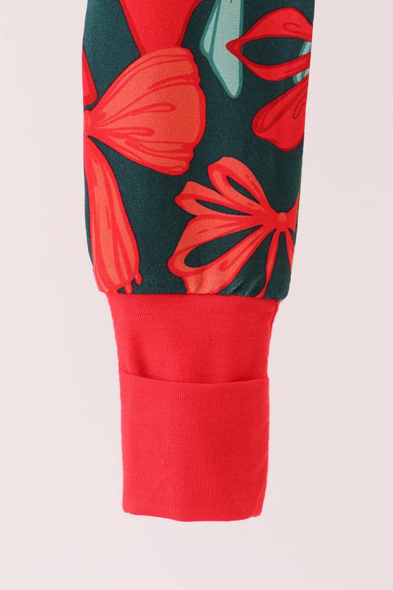 Close-up of a sleeve or cuff showing a dark green fabric with a red and coral floral print, finished with a solid red ribbed cuff pocket on a light pink background.