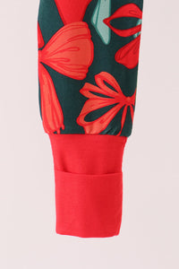 Close-up of a sleeve or cuff showing a dark green fabric with a red and coral floral print, finished with a solid red ribbed cuff pocket on a light pink background.