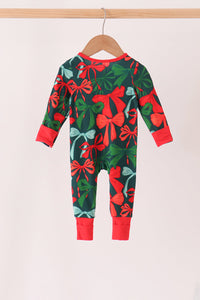 A baby long-sleeve one-piece jumpsuit with a festive Christmas print of red bows, green leaves, and light blue snow globes on a dark green background. It is shown hanging on a wooden hanger against a plain off-white background.