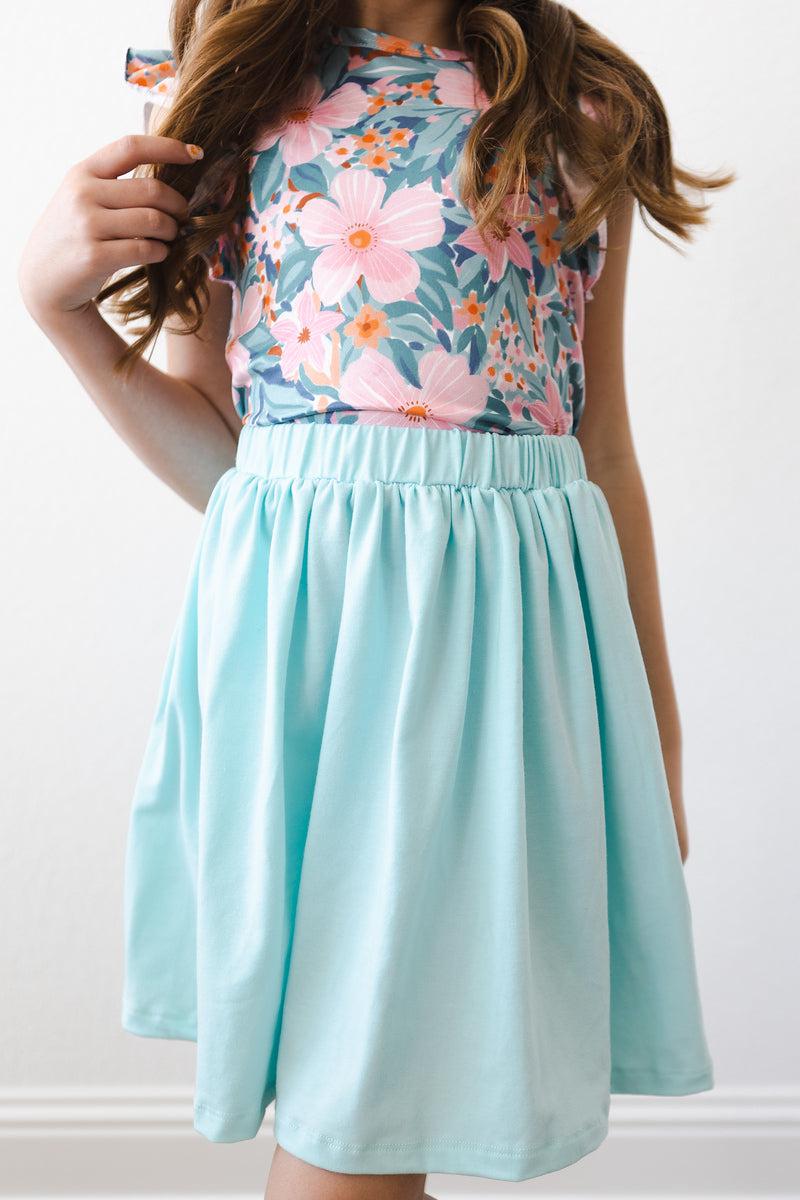 A young girl wearing the Aqua Twirl Skort by Mila & Rose®, showcasing a flowy mint-colored skirt paired with a colorful floral top, perfect for active play and adventures.