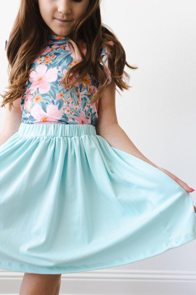 Close-up of a girl wearing the Aqua Twirl Skort by Mila & Rose®, showcasing the vibrant fabric and flattering design paired with a floral top.