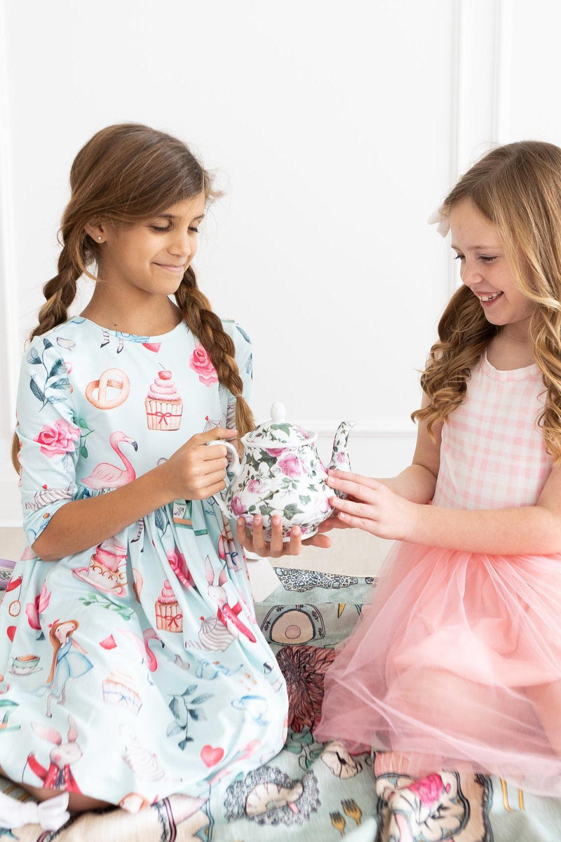 Two girls enjoying a tea party in the Wonderland 3/4 Sleeve Pocket Twirl Dress, showcasing playful designs and vibrant colors, perfect for special occasions and adventures.
