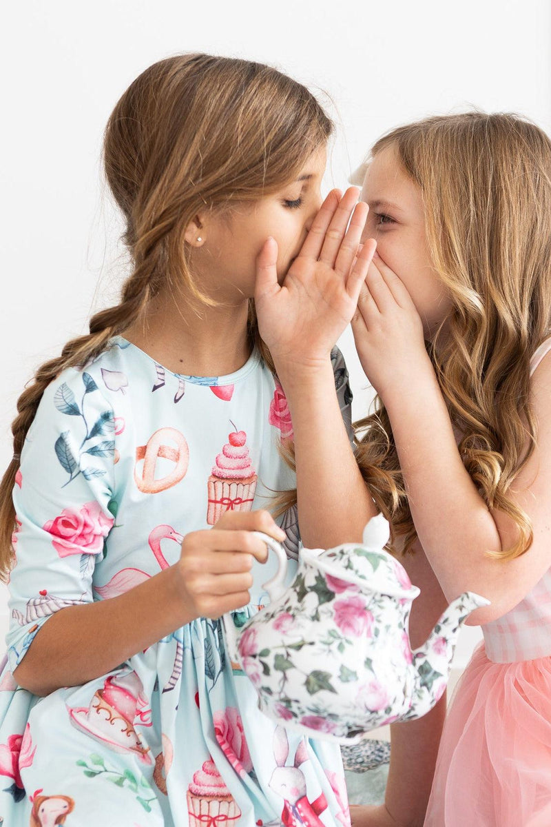 A close-up of two girls sharing secrets while wearing the Wonderland 3/4 Sleeve Pocket Twirl Dress, capturing the joy and charm of childhood in stylish, twirl-worthy attire.