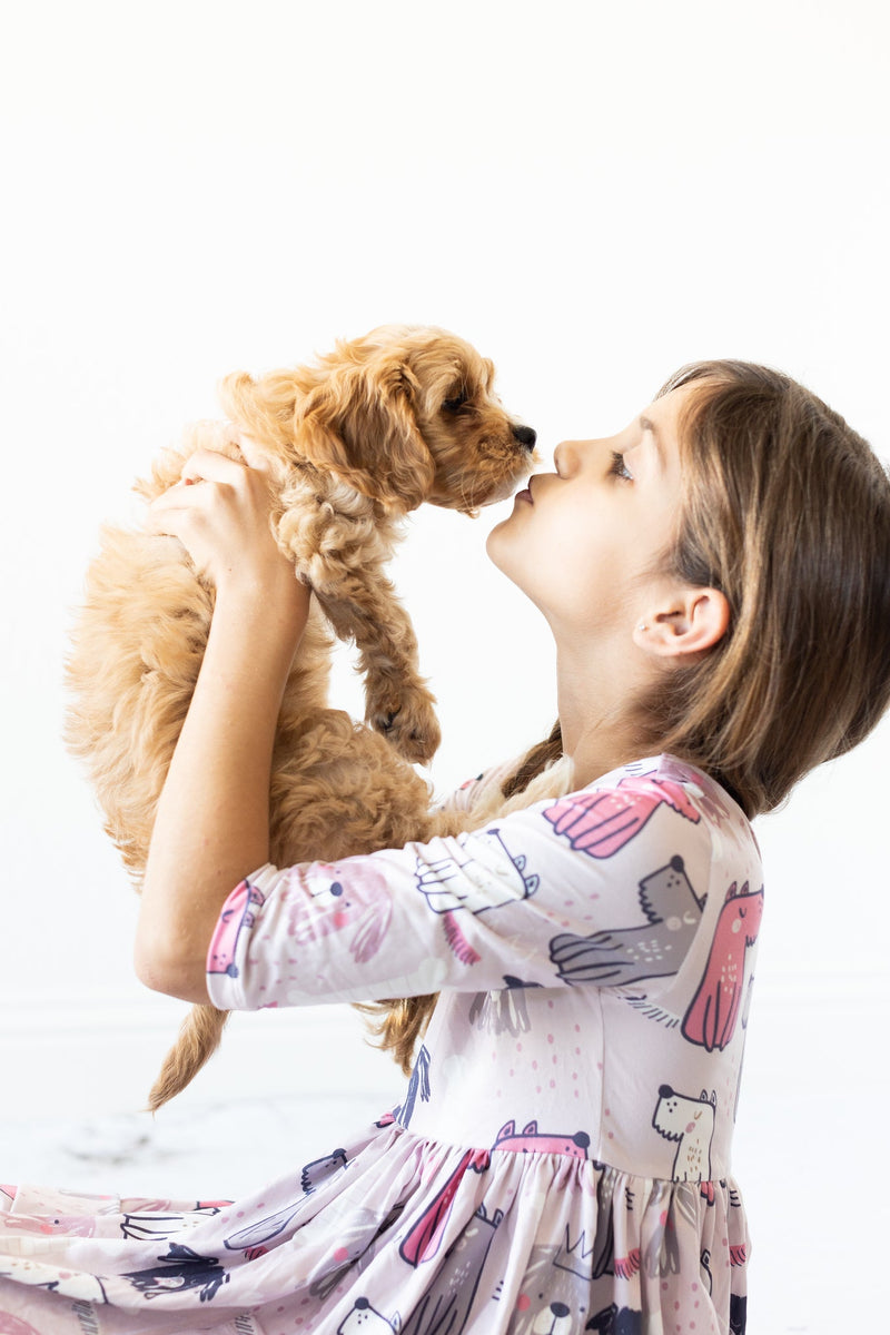A girl in the Adorable Puppy Party 3/4 Sleeve Girls Pocket Twirl Dress shares a kiss with a puppy, highlighting the dress's cute puppy print.