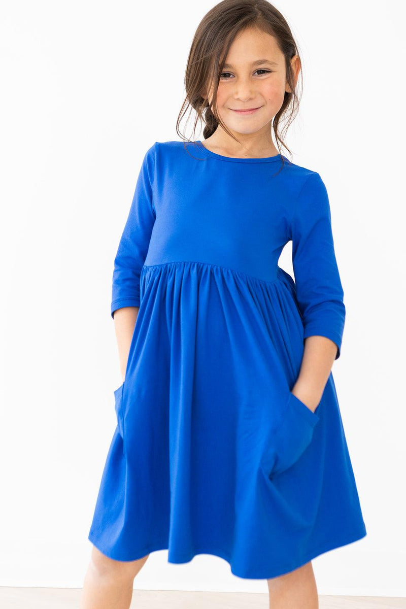 A joyful little girl in the Royal Blue 3/4 Sleeve Pocket Twirl Dress by Mila & Rose, showcasing her twirl-ready style!