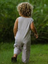 Toddler in Fall Halloween pumpkin-smocked romper, back view, outdoors on grass.