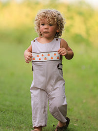 Toddler boy in beige pumpkin-embroidered smocked romper outdoors on a grassy field.