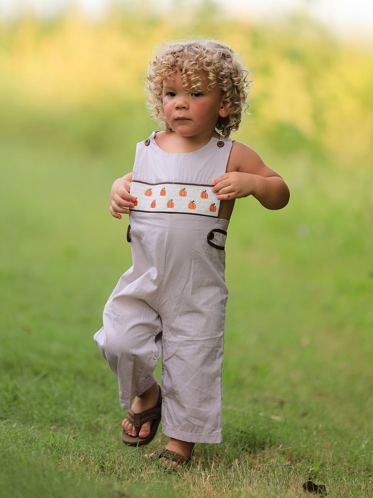 Toddler in a beige pumpkin-embroidered smock romper with chest band, outdoors.