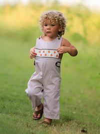 Toddler in a beige pumpkin-embroidered smock romper with chest band, outdoors.