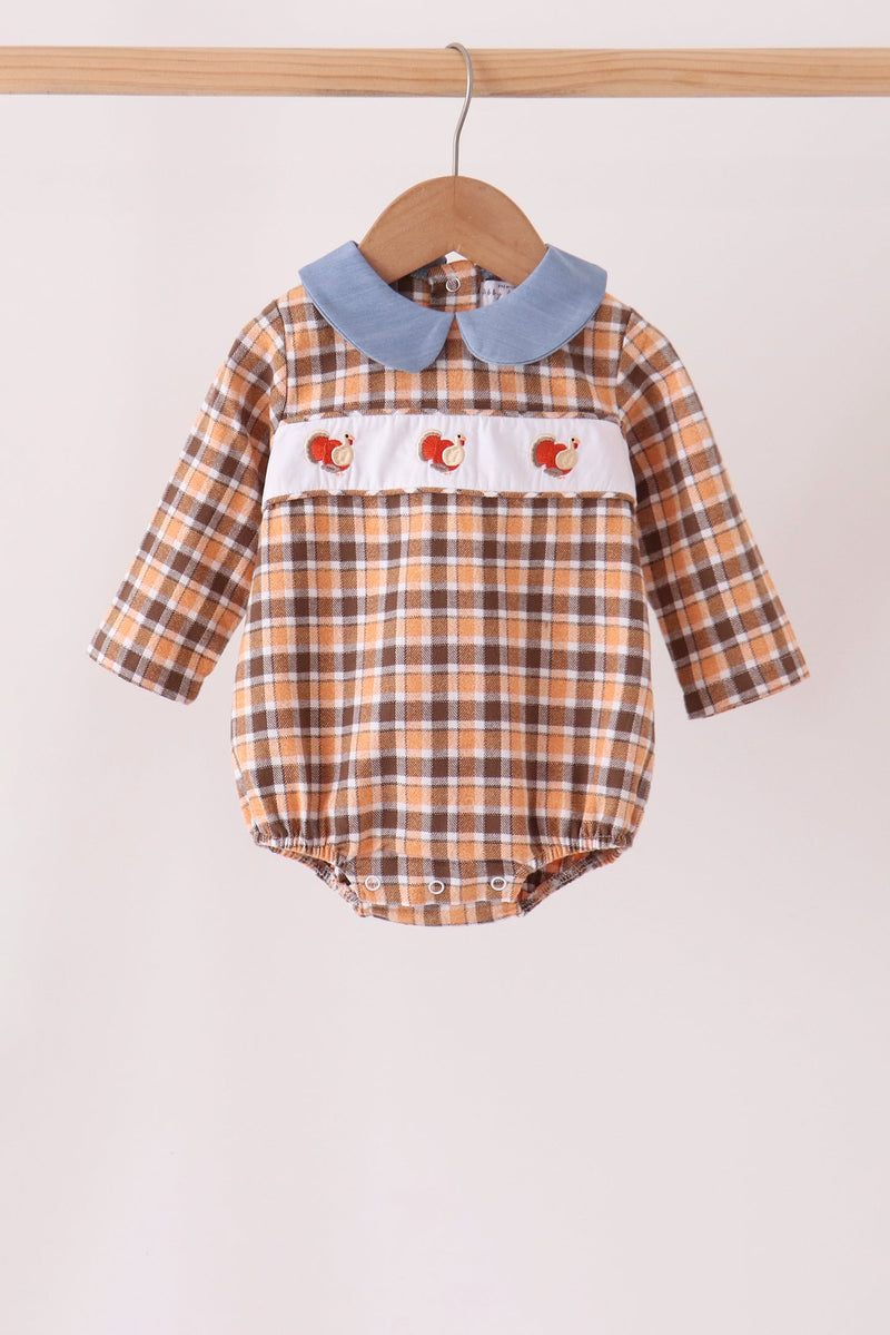 A baby long-sleeve romper with a brown and beige plaid pattern, a light blue denim-style Peter Pan collar, and a white chest band featuring embroidered red and orange foxes, hanging on a wooden hanger against a plain light background.