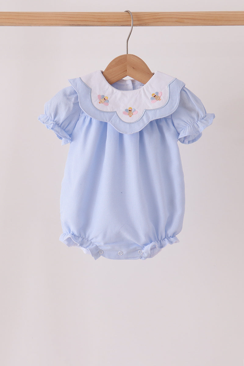 A light blue baby romper with a white ruffled collar featuring embroidered pastel flowers, hanging on a wooden hanger against a plain light beige background.