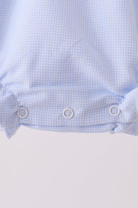 Close-up of a light blue and white gingham fabric garment with three silver metal snap buttons along the bottom hem, set against a plain light background.