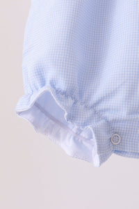 Close-up of a light blue and white gingham fabric garment, showing a ruffled cuff and a small metal snap button.