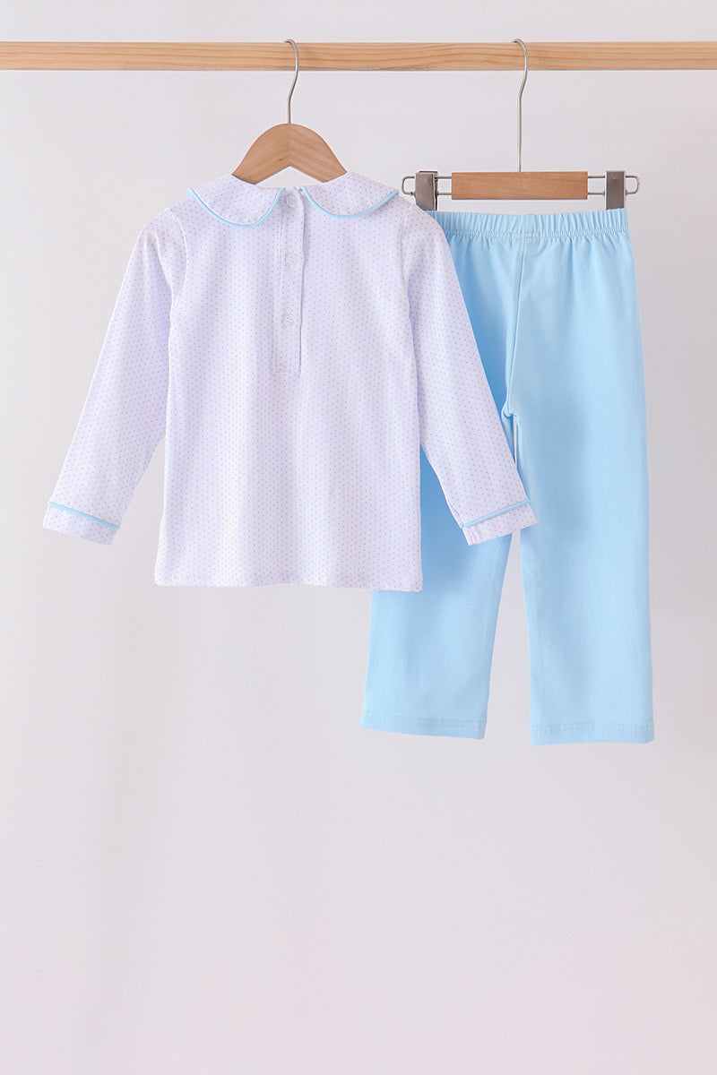 A two-piece children's outfit hanging on wooden hangers against a plain light background. The set includes a white long-sleeve top with a small pink polka dot pattern and light blue collar/cuff trim, paired with light blue pants.