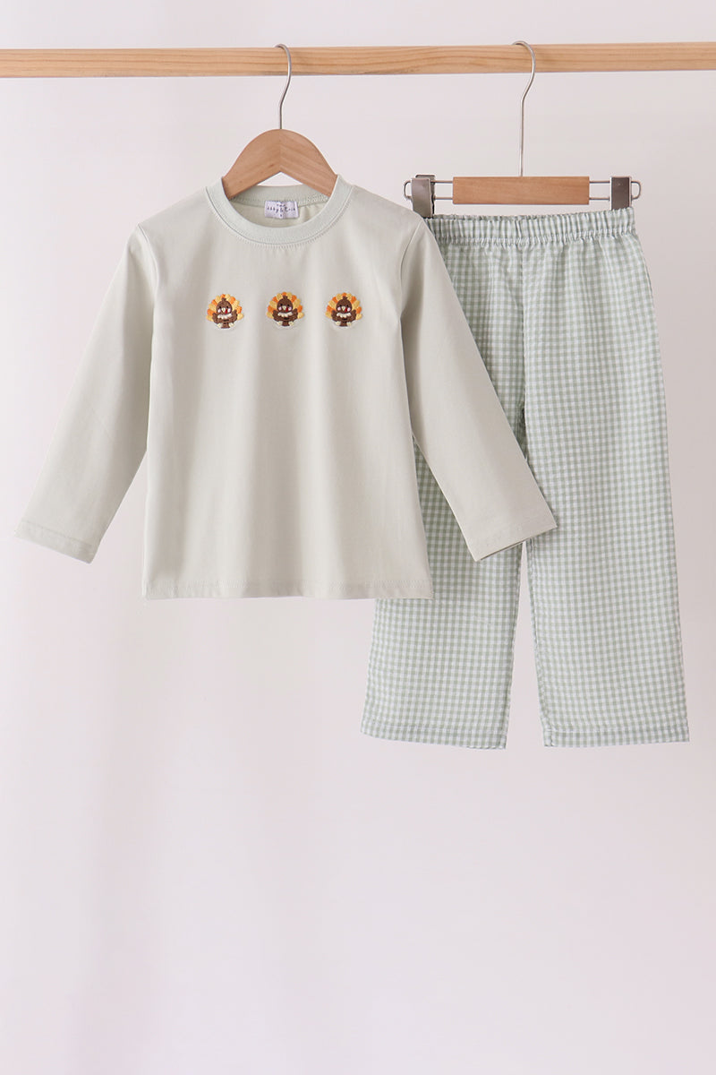 A children's two-piece pajama set hanging on wooden hangers against a plain light background. The set includes a long-sleeve top in a pale sage green with three small embroidered tiger faces on the chest, and matching checkered pants in a light green and white gingham pattern.