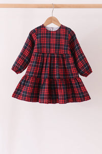 A toddler girl's long-sleeve dress in a red and black plaid pattern, hanging on a wooden hanger against a plain white wall.