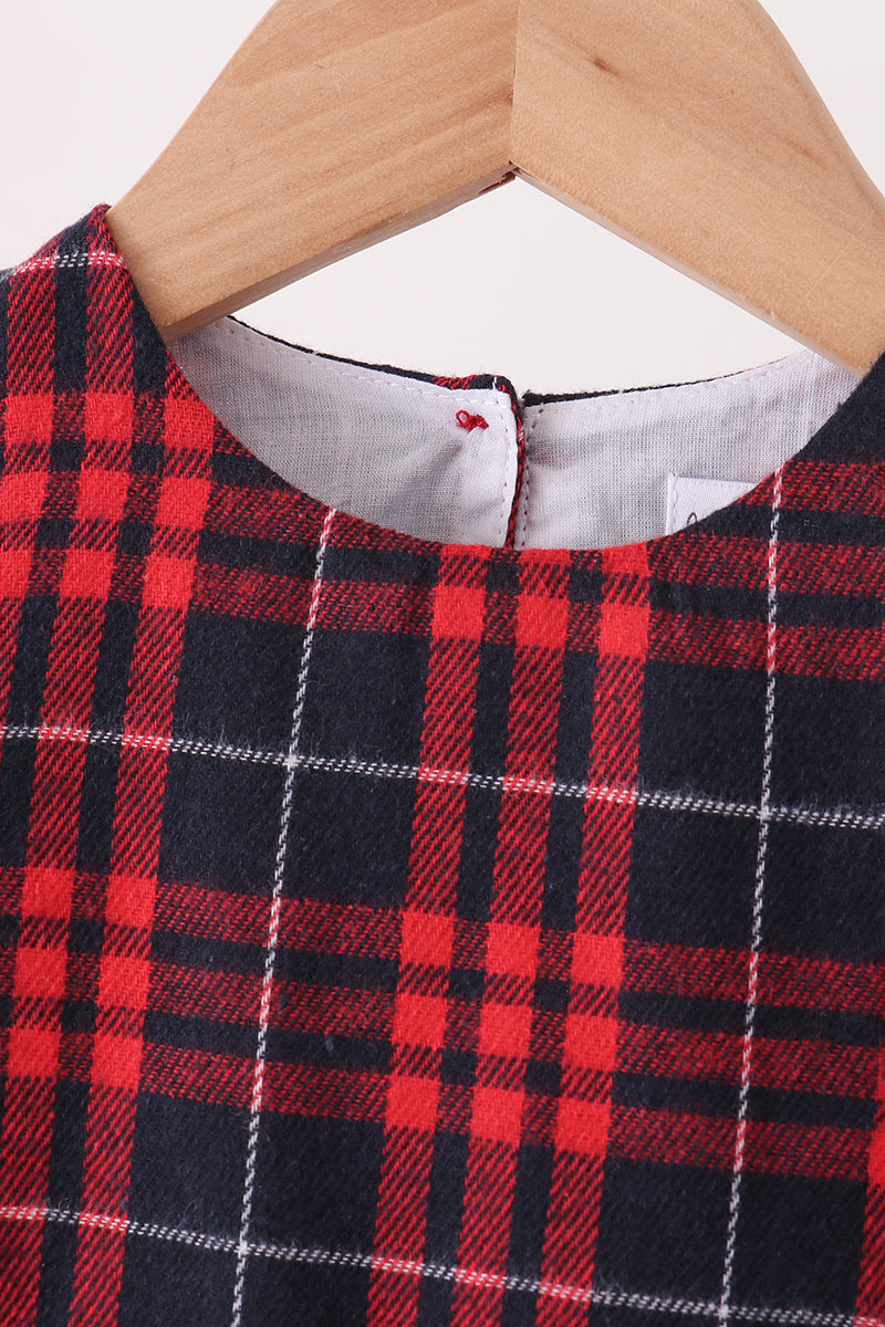A close-up of a red and navy plaid garment hanging on a light wood hanger against a plain light background.