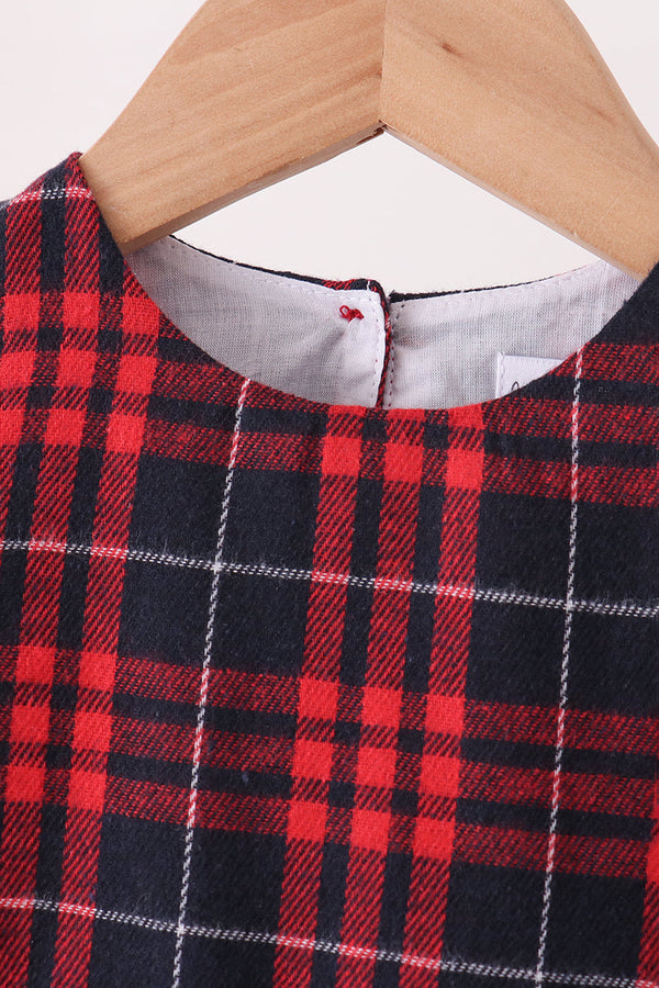 A close-up of a red and navy plaid garment hanging on a light wood hanger against a plain light background.