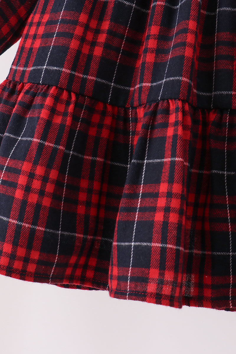 Close-up of a red and black plaid fabric garment, showing a tiered ruffle hem with thin white intersecting lines in the plaid pattern.