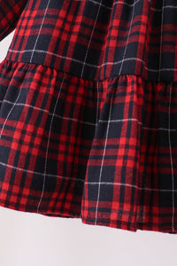 Close-up of a red and black plaid fabric garment, showing a tiered ruffle hem with thin white intersecting lines in the plaid pattern.