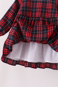 A close-up of a red and black plaid long-sleeve dress with a ruffled waist and a white ruffled underskirt visible underneath, set against a plain light background.