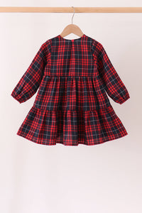 A toddler girl's long-sleeve tiered dress in a red and black plaid pattern, hanging on a wooden hanger from a light wood clothing rack against a plain off-white background.