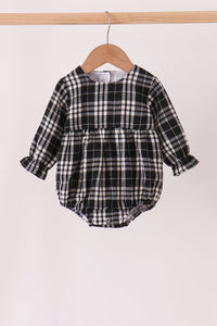 A baby long-sleeve plaid romper in black and white, hanging on a wooden hanger from a light wood clothing rack against a plain off-white background.