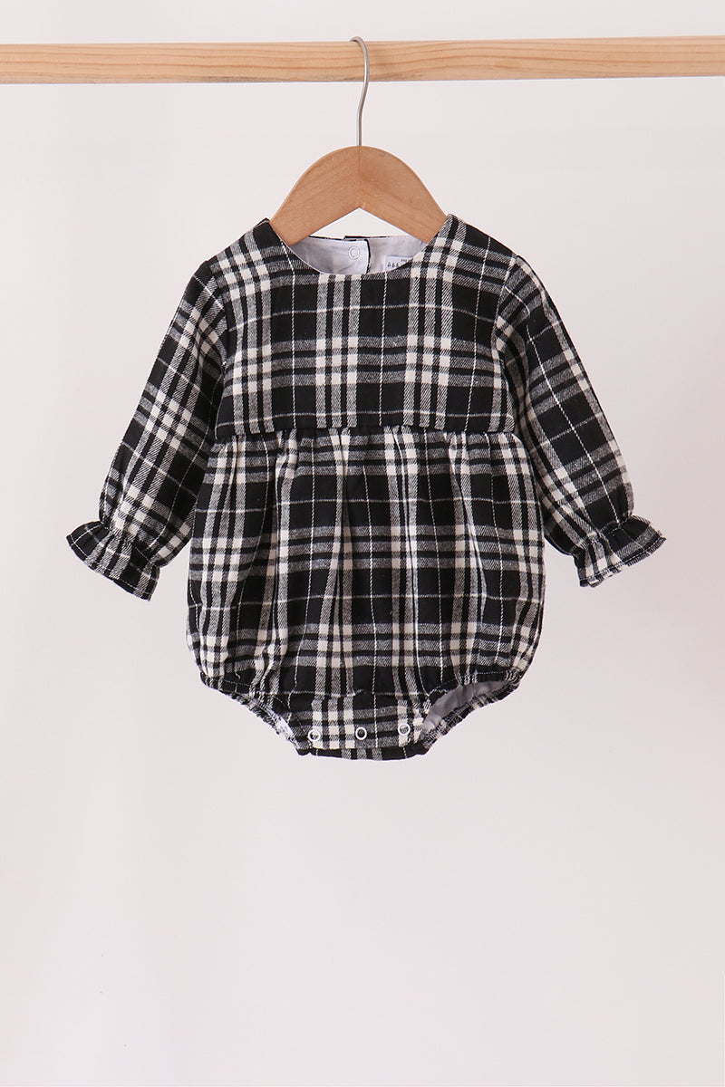 A baby long-sleeve plaid romper in black and white, hanging on a wooden hanger from a light wood clothing rack against a plain off-white background.