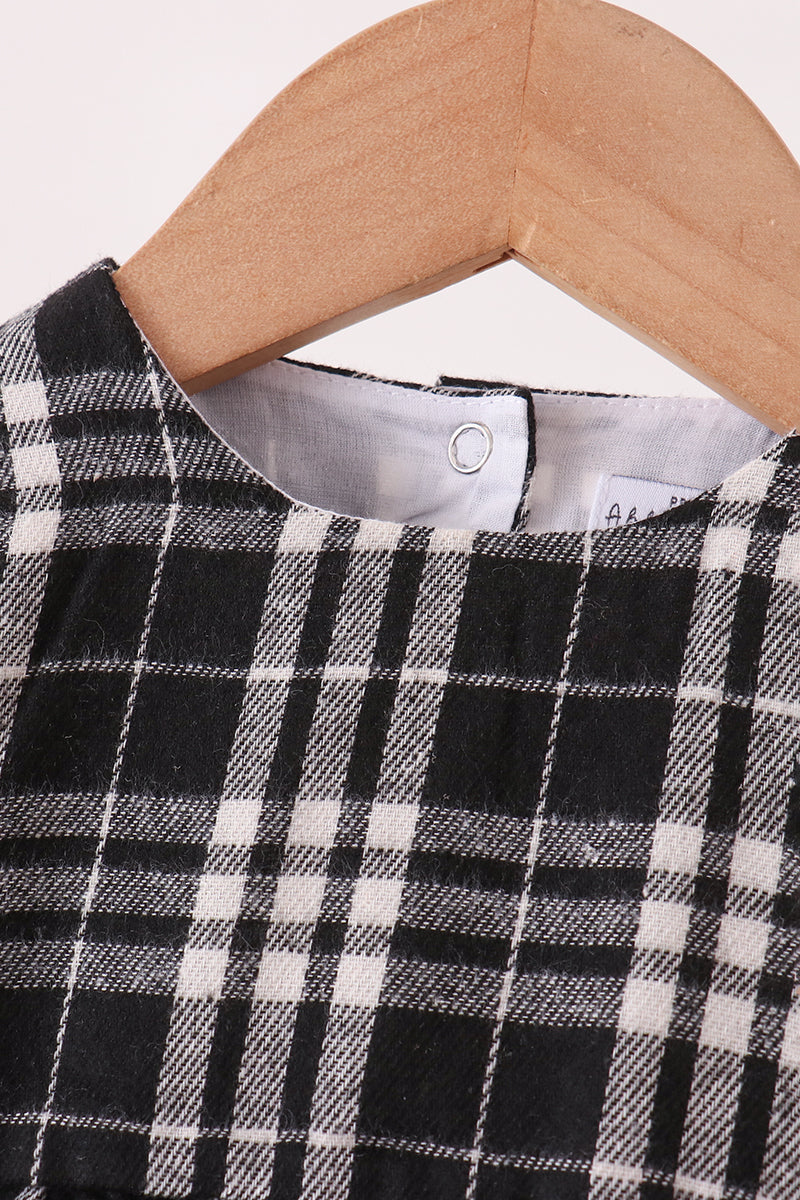 A close-up of a black and white plaid garment hanging on a light wood hanger against a plain light background.