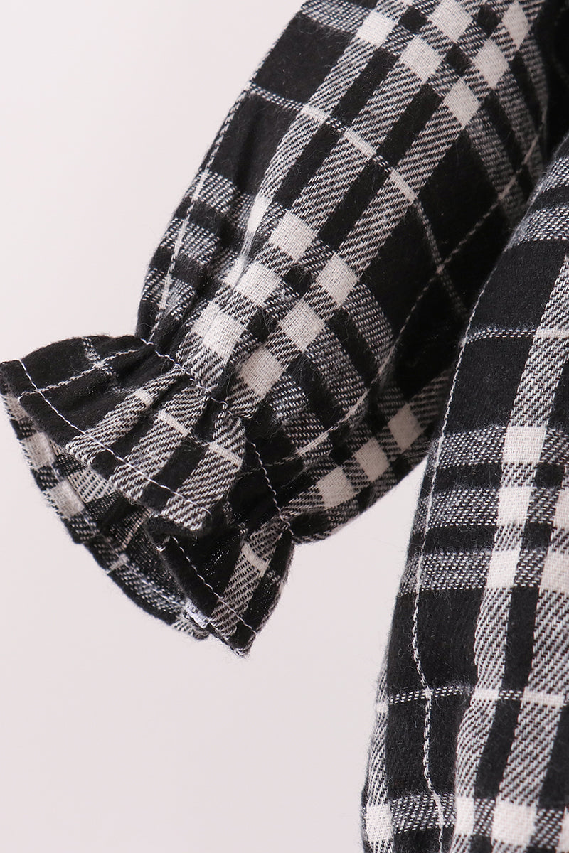 Close-up of a black and white plaid garment sleeve with a gathered ruffled cuff, showing the fabric texture and pattern.