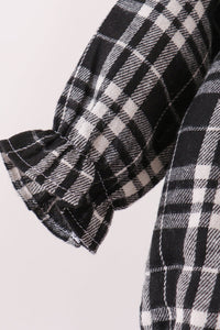 Close-up of a black and white plaid garment sleeve with a gathered ruffled cuff, showing the fabric texture and pattern.