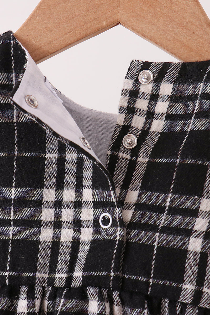 Close-up of a black and white plaid garment on a wooden hanger, showing a buttoned neckline with a light gray inner lining.
