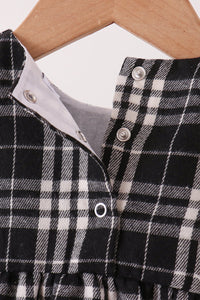 Close-up of a black and white plaid garment on a wooden hanger, showing a buttoned neckline with a light gray inner lining.