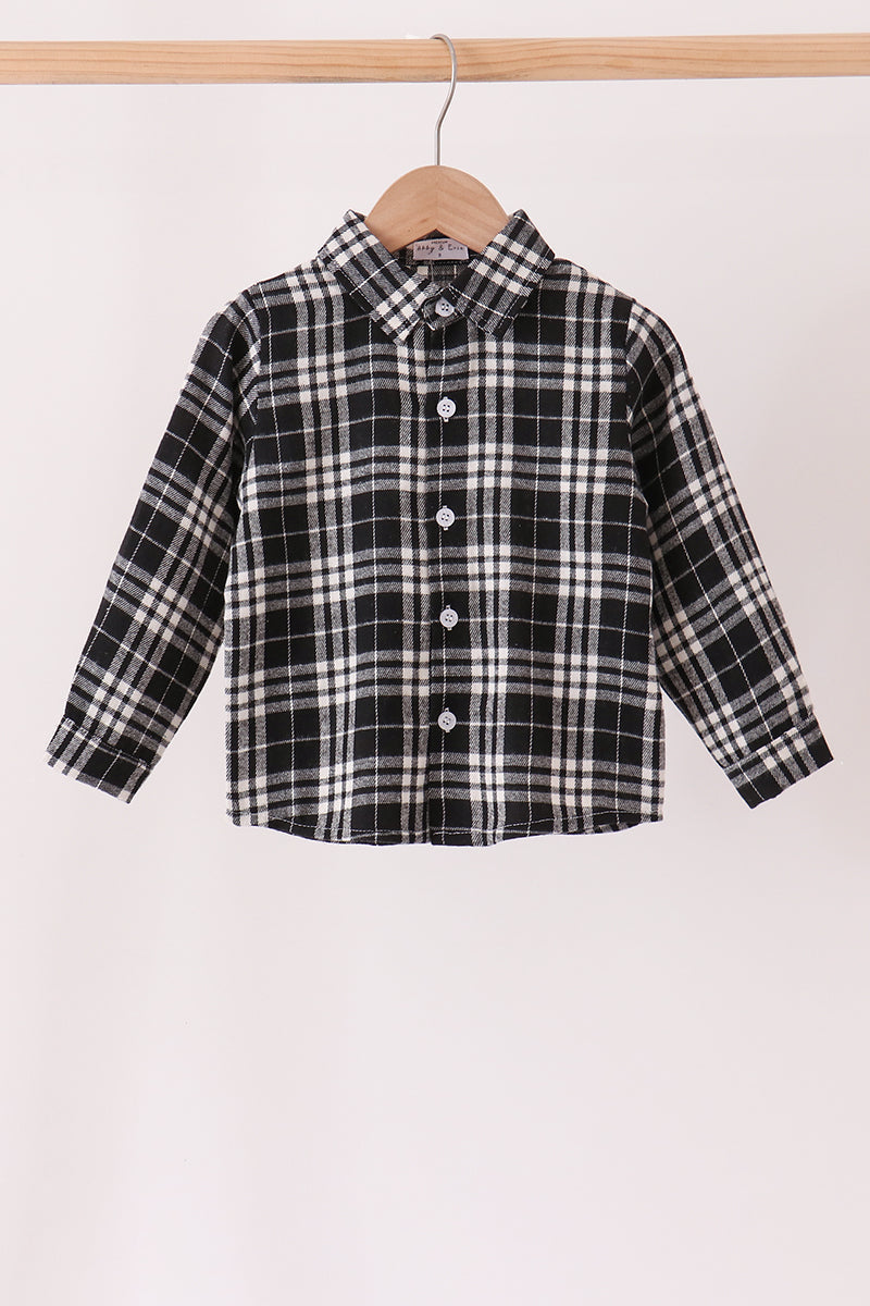 A long-sleeve children's button-up shirt with a black and white plaid pattern, hanging on a wooden hanger from a light wood clothes rack against a plain off-white background.