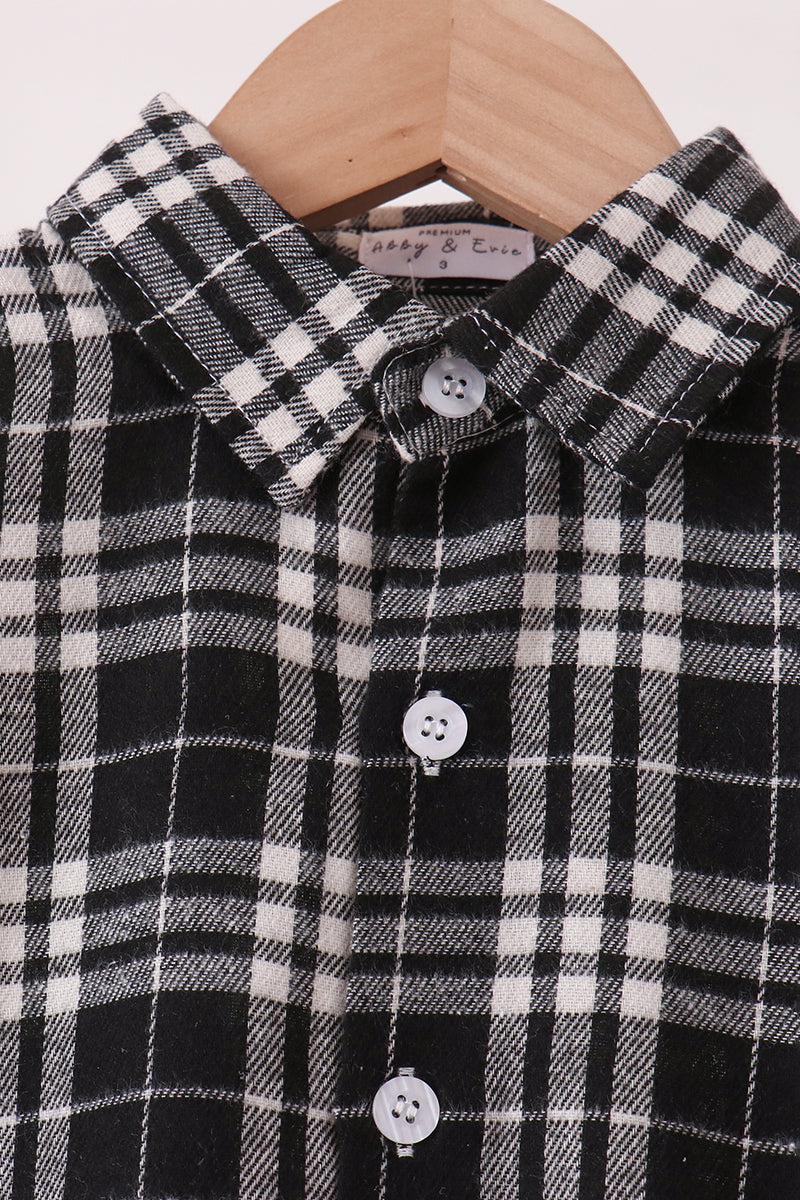 A close-up of a black and white plaid button-down shirt hanging on a wooden hanger. The shirt features a classic checkered pattern with white buttons.