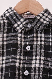 A close-up of a black and white plaid button-down shirt hanging on a wooden hanger. The shirt features a classic checkered pattern with white buttons.