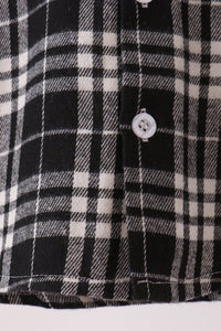 Close-up of a black and white plaid button-down shirt fabric, showing the weave pattern and a white button.