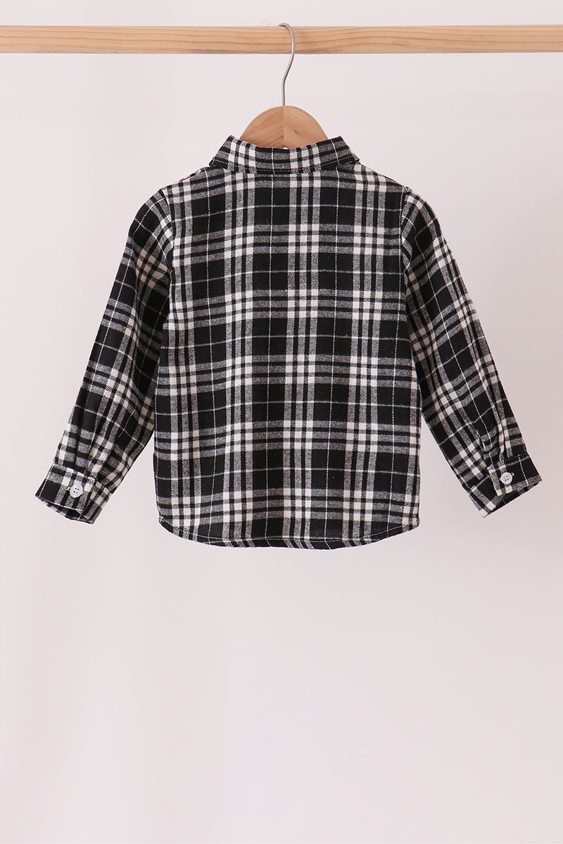 A long-sleeve plaid button-up shirt in black, white, and gray, hanging on a wooden hanger from a light wood clothing rack against a plain off-white background.