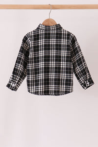 A long-sleeve plaid button-up shirt in black, white, and gray, hanging on a wooden hanger from a light wood clothing rack against a plain off-white background.