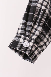 Close-up of a black and white plaid shirt sleeve with a single white button on the cuff, set against a plain off-white background.