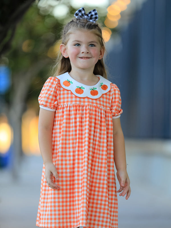 Girl wearing orange gingham puff sleeve dress with pumpkin embroidered collar and black white buffalo check bow.