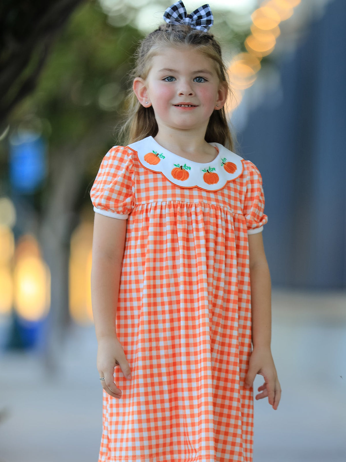 Orange gingham puff sleeve dress for girls with pumpkin-embroidered fan neckline and matching buffalo check hair bow.
