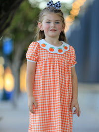 Orange gingham puff sleeve dress for girls with pumpkin-embroidered fan neckline and matching buffalo check hair bow.
