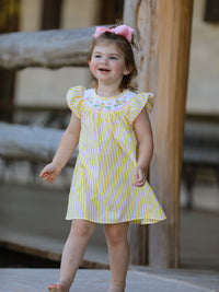 Young girl wearing a yellow striped dress with pink bow, embroidered chick floral design on the yoke.