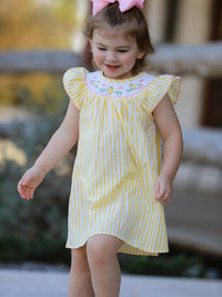 Young girl in a yellow-and-white striped smocked dress with chick floral embroidery on the yoke.