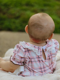 Back view of baby girl in pink plaid romper with lace collar and button keyhole detail.